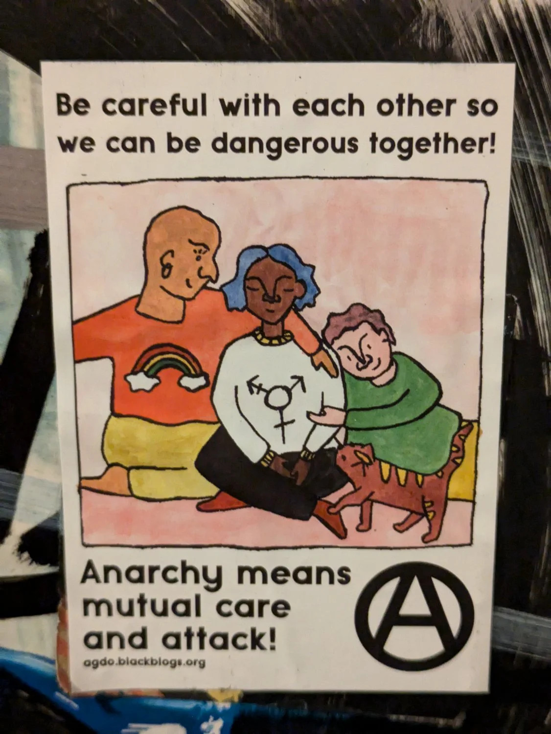 Sticker with image of 3 people and a cat cuddling, with text "Be careful with each other so we can be dangerous together" above and the text "Anarchy means mutual care and attack!" below next to an circle A.