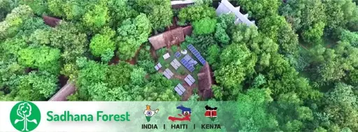 Picture of sadhana forest an aerial view of forest with solar panels in between along with huts.